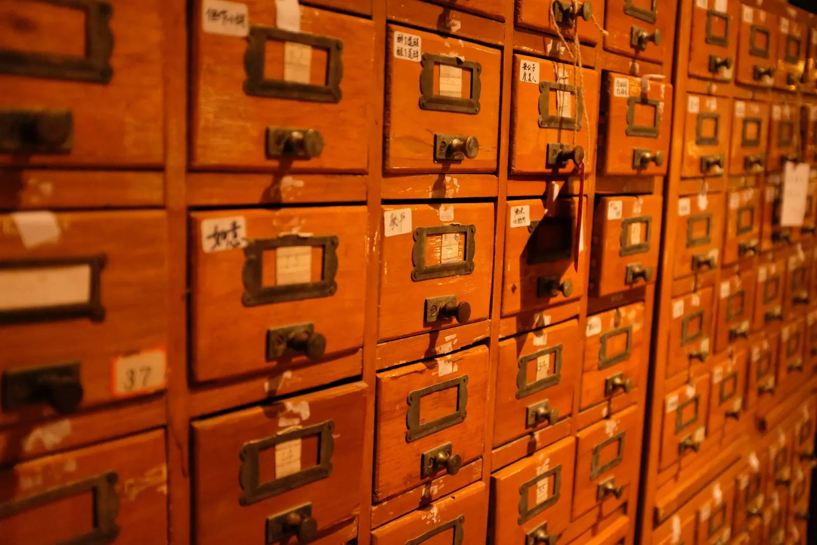 A wall of vintage wooden card catalogue drawers with brass label holders - a record that is indexed, permanently retrievable and cannot be amended once filed